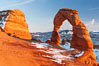 Delicate Arch, dusted with snow, at sunset, with the snow-covered La Sal mountains in the distance.  Delicate Arch stands 45 feet high, with a span of 33 feet, atop of bowl of slickrock sandstone. Arches National Park, Utah, USA