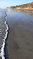 Ocean water washes over a flat sand beach, sandstone bluffs rise in the background, sunset. Carlsbad, California, USA. Image #19805