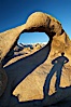 The long shadow of a hiker lies on Mobius Arch, a natural stone arch in the Alabama Hills. Alabama Hills Recreational Area, California, USA. Image #21733