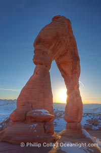 Delicate Arch, dusted with snow, at sunset, with the snow-covered La Sal mountains in the distance.  Delicate Arch stands 45 feet high, with a span of 33 feet, atop of bowl of slickrock sandstone, Arches National Park, Utah