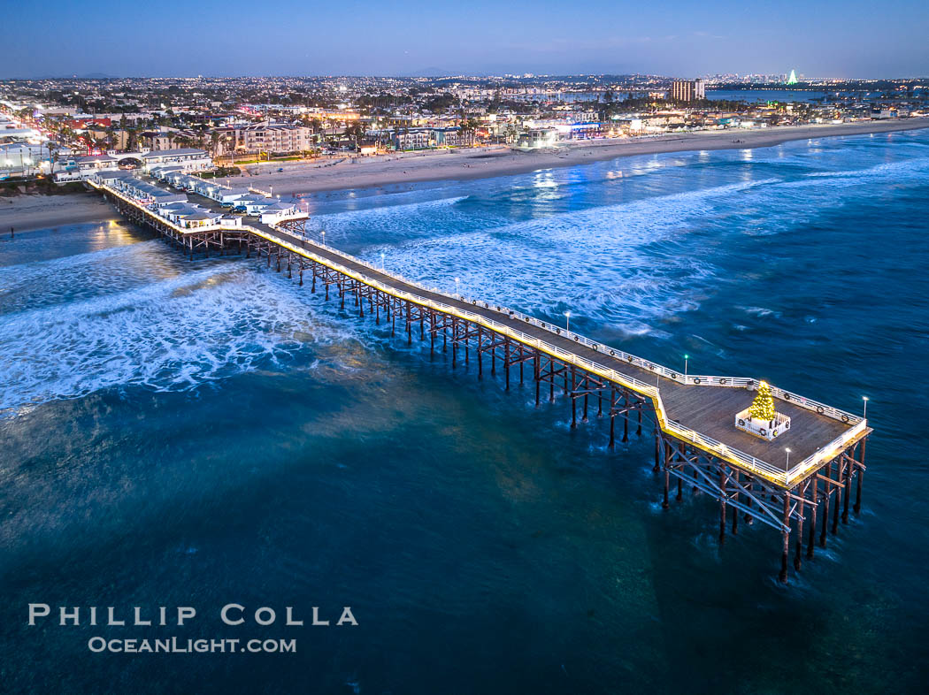 Aerial photo of Crystal Pier with Holiday Christmas Lights at night. The Crystal Pier, Holiday Lights and Pacific Ocean at sunset, waves blur as they crash upon the sand. Crystal Pier, 872 feet long and built in 1925, extends out into the Pacific Ocean from the town of Pacific Beach. California, USA, natural history stock photograph, photo id 39999