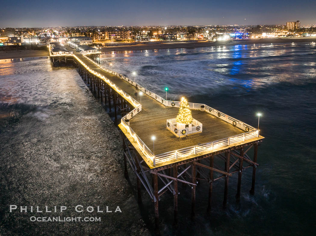 Aerial photo of Crystal Pier with Holiday Christmas Lights at night. The Crystal Pier, Holiday Lights and Pacific Ocean at sunset, waves blur as they crash upon the sand. Crystal Pier, 872 feet long and built in 1925, extends out into the Pacific Ocean from the town of Pacific Beach. California, USA, natural history stock photograph, photo id 40003