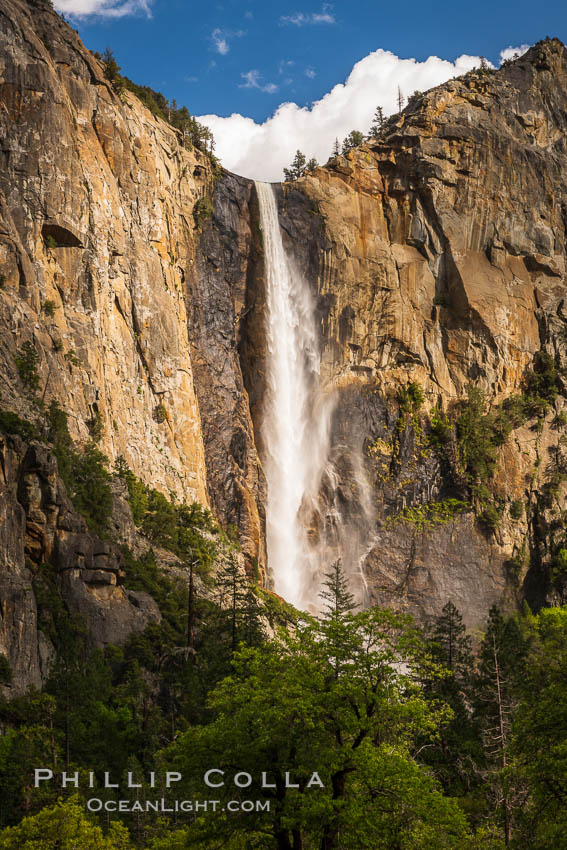 Bridalveil Falls at sunset, with clouds and blue sky in the background. Bridalveil Falls in Yosemite drops 620 feet (188 m) from a hanging valley to the floor of Yosemite Valley, Yosemite National Park, California