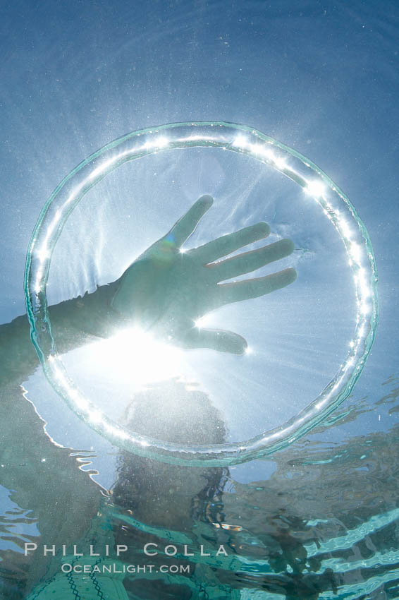 A bubble ring. A child puts her hand through a bubble ring at it ascends through the water toward her