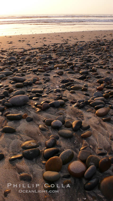 Cobblestones on a flat sand beach.  Cobble stones are polished round and smooth by years of wave energy.  They are alternately exposed and covered by sand depending on the tides, waves and seasons of the year.  Cobblestones are common on the beaches of southern California, contained in the sandstone bluffs along the beach and released onto the beach as the bluffs erode, Carlsbad