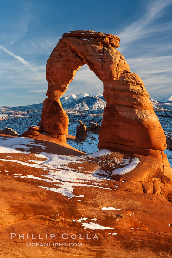 Delicate Arch, dusted with snow, at sunset, with the snow-covered La Sal mountains in the distance.  Delicate Arch stands 45 feet high, with a span of 33 feet, atop of bowl of slickrock sandstone. Arches National Park, Utah, USA, natural history stock photograph, photo id 18111