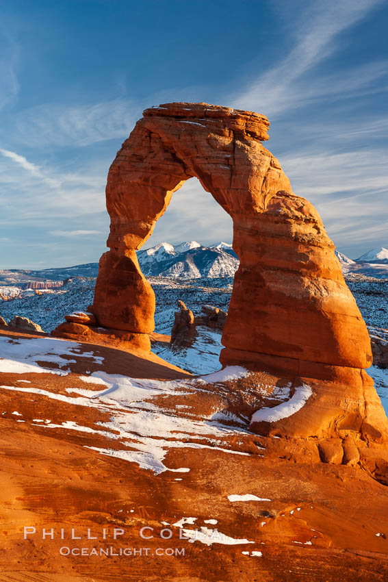 Delicate Arch, dusted with snow, at sunset, with the snow-covered La Sal mountains in the distance.  Delicate Arch stands 45 feet high, with a span of 33 feet, atop of bowl of slickrock sandstone. Arches National Park, Utah, USA, natural history stock photograph, photo id 18105