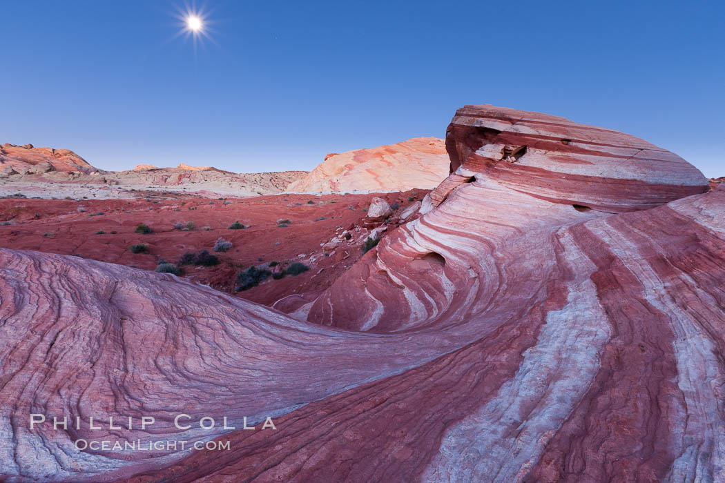 The moon sets over the Fire Wave, a beautiful sandstone formation exhibiting dramatic striations, striped layers in the geologic historical record, Valley of Fire State Park