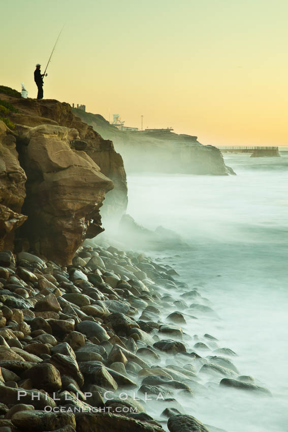 Fisherman at dawn along the La Jolla coastline, waves blur as they crash upon the Boomer Beach boulders