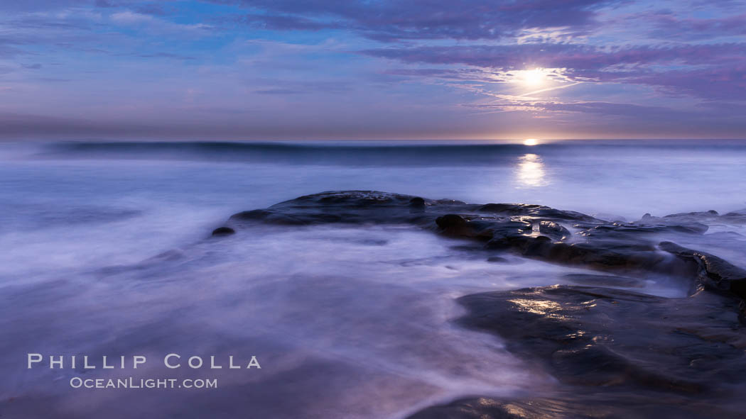 Breaking waves crash upon a rocky reef under the light of a full moon, La Jolla, California