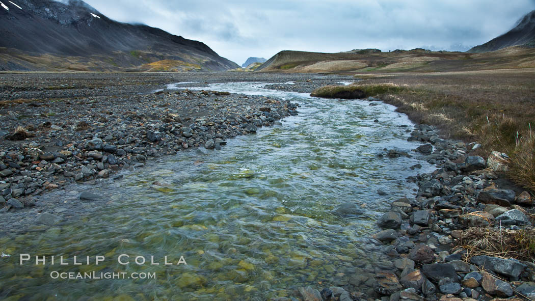 Glacial melt waters, runoff, flows across an alluvial flood plain between mountains, on its way to Stromness Bay, Stromness Harbour