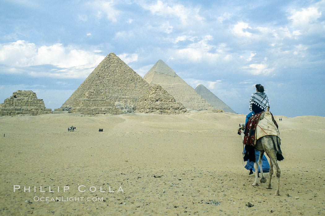 Great pyramids, visitor rides a camel across the sands to see the pyramids, Egypt.  Pyramids of Queens, Pyramid of Menkaure, Pyramid of Khafre, Pyramid of Khufu (left to right, front to back), Giza