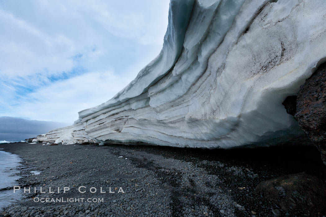 Horizontal striations and layers in packed snow, melting and overhanging, seen from the edge of the snowpack, along a rocky beach, Brown Bluff