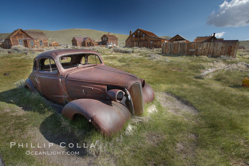 Old car lying in dirt field, Fuller Street and Green Street buildings in background. Bodie State Historical Park, California, USA, natural history stock photograph, photo id 23134