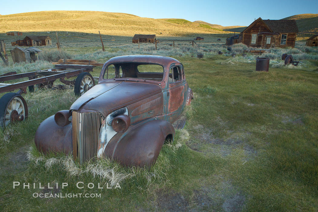 Old car lying in dirt field, Fuller Street and Green Street buildings in background. Bodie State Historical Park, California, USA, natural history stock photograph, photo id 23164