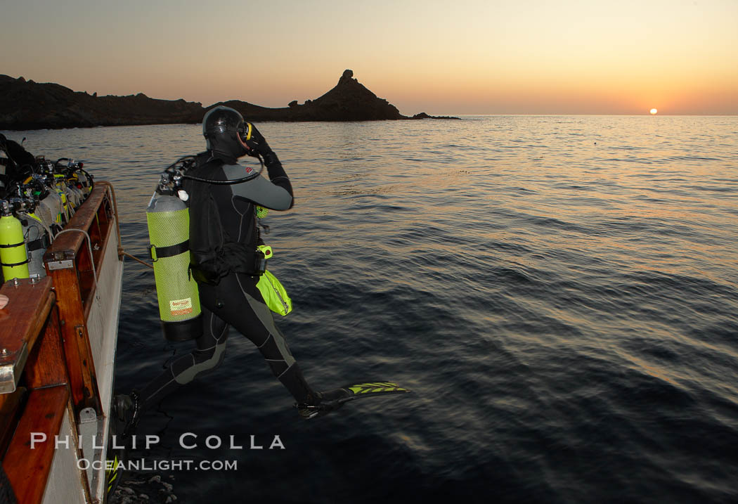 A SCUBA diver leaps into the water, from boat Horizon, into the kelp forest and rich waters of San Clemente Island, China Hat Point, Balanced Rock, sunrise