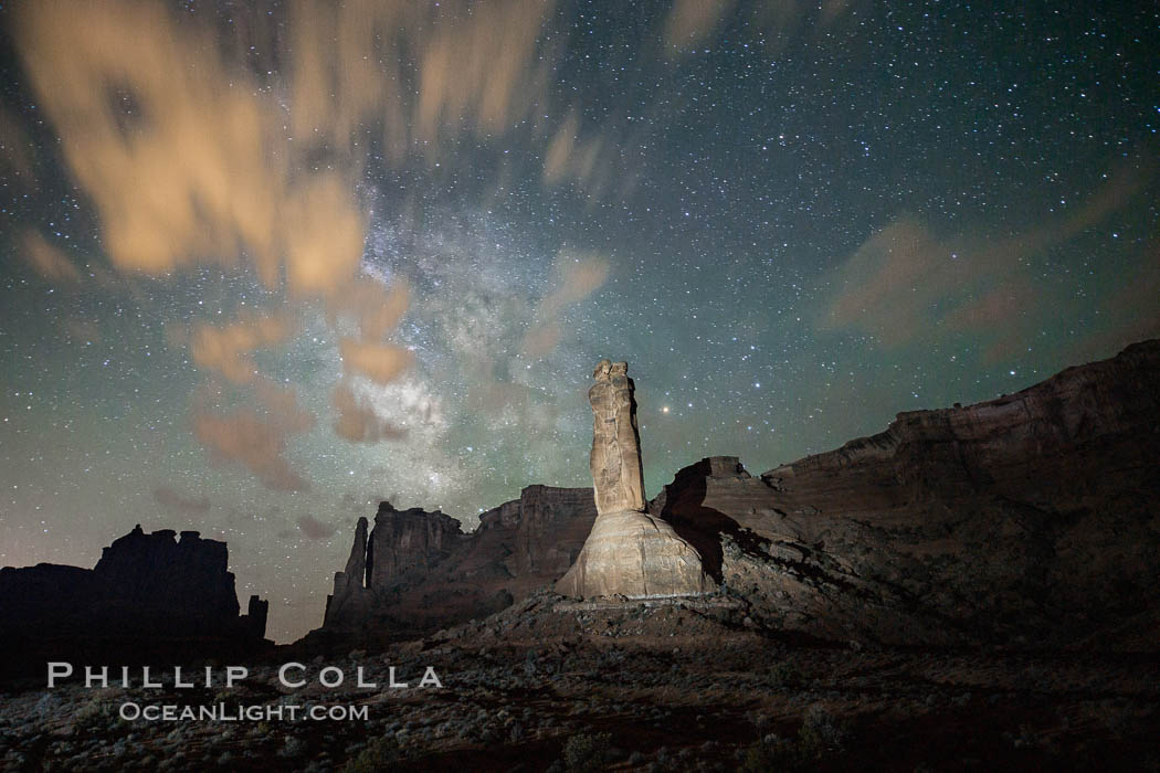 Stone columns rising in the night sky, milky way and stars and clouds filling the night sky overhead, Arches National Park, Utah