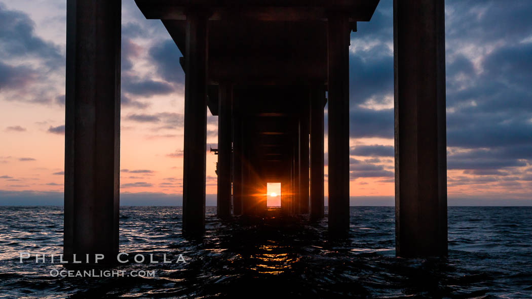 Scripps Pier solstice, surfer's view from among the waves, sunset aligned perfectly with the pier. Research pier at Scripps Institution of Oceanography SIO, sunset, La Jolla, California