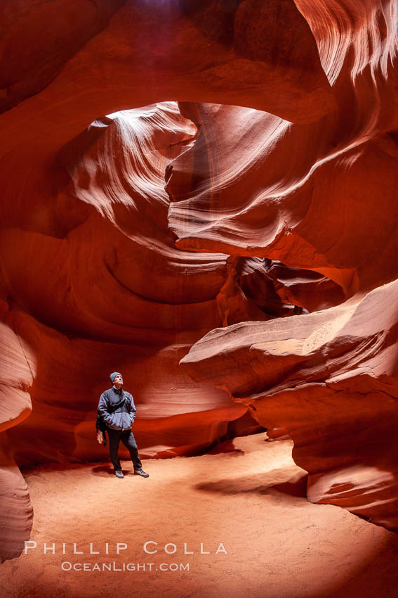 A hiker admiring the striated walls and dramatic light within Antelope Canyon, a deep narrow slot canyon formed by water and wind erosion, Navajo Tribal Lands, Page, Arizona