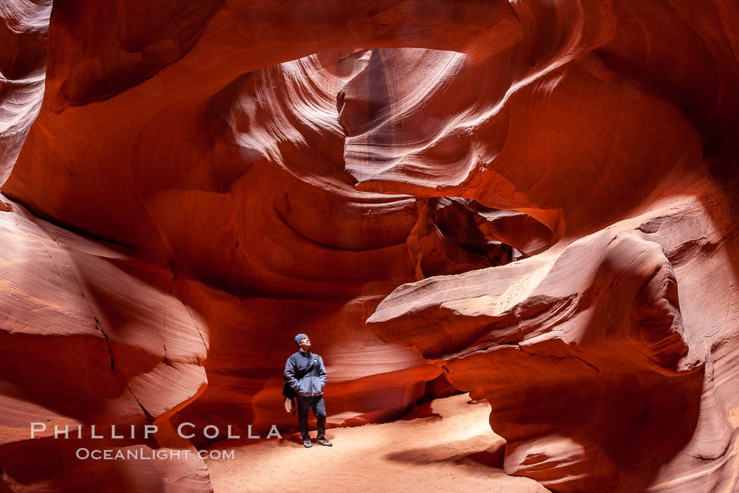 A hiker admiring the striated walls and dramatic light within Antelope Canyon, a deep narrow slot canyon formed by water and wind erosion, Navajo Tribal Lands, Page, Arizona