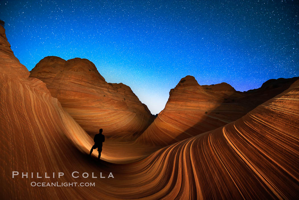 The Wave at Night, under a clear night sky full of stars. Photographer is illuminating the striated rocks with a small handheld light. The Wave, an area of fantastic eroded sandstone featuring beautiful swirls, wild colors, countless striations, and bizarre shapes set amidst the dramatic surrounding North Coyote Buttes of Arizona and Utah. The sandstone formations of the North Coyote Buttes, including the Wave, date from the Jurassic period. Managed by the Bureau of Land Management, the Wave is located in the Paria Canyon-Vermilion Cliffs Wilderness and is accessible on foot by permit only