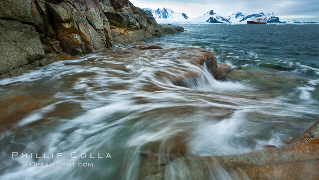 Waves rush in, sunset, Antarctica.  Ocean water rushes ashore over the rocky edge of Peterman Island, Antarctica