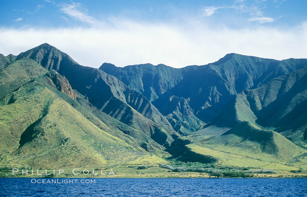 West Maui mountains rise above the coast of Maui, with clouds flanking the ancient eroded remnants of a volcano