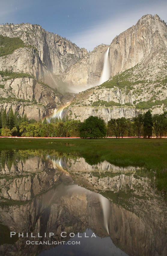 Yosemite Falls by moonlight, reflected in a springtime pool in Cooks Meadow. A lunar rainbow (moonbow) can be seen above the lower section of Yosemite Falls. Star trails appear in the night sky. Yosemite Valley, Yosemite National Park, California