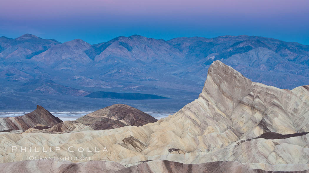 Zabriskie Point, sunrise.  Manly Beacon rises in the center of an eroded, curiously banded area of sedimentary rock, with the Panamint Mountains visible in the distance, Death Valley National Park, California
