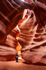 A hiker admiring the striated walls and dramatic light within Antelope Canyon, a deep narrow slot canyon formed by water and wind erosion. Navajo Tribal Lands, Page, Arizona, USA. Image #17996