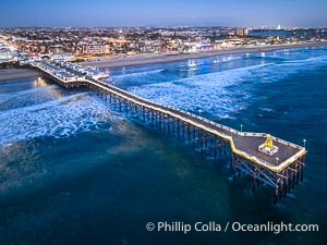 Aerial photo of Crystal Pier with Holiday Christmas Lights at night. The Crystal Pier, Holiday Lights and Pacific Ocean at sunset, waves blur as they crash upon the sand. Crystal Pier, 872 feet long and built in 1925, extends out into the Pacific Ocean from the town of Pacific Beach