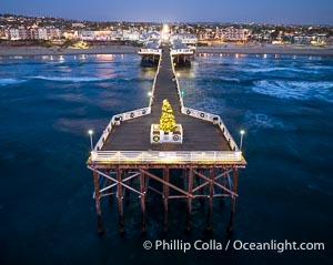 Aerial photo of Crystal Pier with Holiday Christmas Lights at night. The Crystal Pier, Holiday Lights and Pacific Ocean at sunset, waves blur as they crash upon the sand. Crystal Pier, 872 feet long and built in 1925, extends out into the Pacific Ocean from the town of Pacific Beach