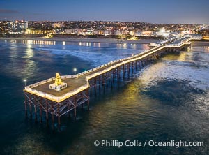 Aerial photo of Crystal Pier with Holiday Christmas Lights at night. The Crystal Pier, Holiday Lights and Pacific Ocean at sunset, waves blur as they crash upon the sand. Crystal Pier, 872 feet long and built in 1925, extends out into the Pacific Ocean from the town of Pacific Beach