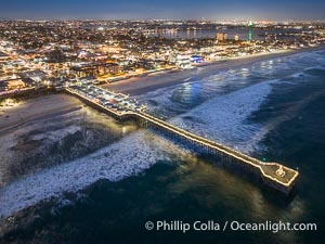 Aerial photo of Crystal Pier with Holiday Christmas Lights at night. The Crystal Pier, Holiday Lights and Pacific Ocean at sunset, waves blur as they crash upon the sand. Crystal Pier, 872 feet long and built in 1925, extends out into the Pacific Ocean from the town of Pacific Beach