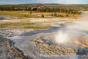 Anemone Geyser erupts, Old Faithful Inn visible in the distance.  Anemone Geyser cycles about every 7 minutes.  First the pools fills, then overflows, then bubbles and splashes before erupting.  The eruption empties the pools and the cycle begins anew.  Upper Geyser Basin, Yellowstone National Park, Wyoming