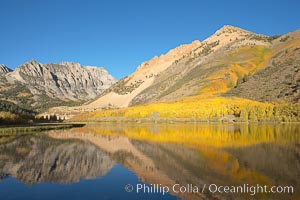 Aspens changing into fall colors, yellow and orange, are reflected in North Lake in October, Bishop Creek Canyon, Eastern Sierra.