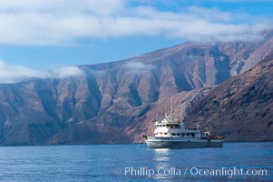 Guadalupe Islands mountainous terrain and sea cliffs tower above the dive boat Horizon while at anchor in Spanish Cove, near the north end of Guadalupe Island (Isla Guadalupe)