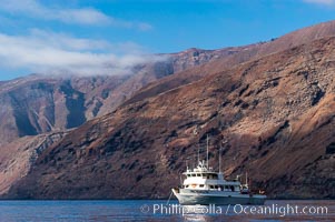 Guadalupe Islands mountainous terrain and sea cliffs tower above the dive boat Horizon while at anchor in Spanish Cove, near the north end of Guadalupe Island (Isla Guadalupe)