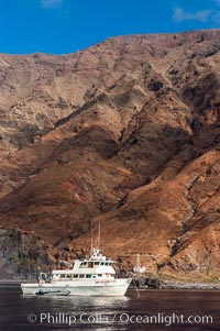 Guadalupe Islands mountainous terrain and sea cliffs tower above the dive boat Horizon while at anchor in Spanish Cove, near the north end of Guadalupe Island (Isla Guadalupe)