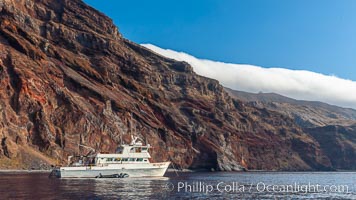 Guadalupe Islands mountainous terrain and sea cliffs tower above the dive boat Horizon while at anchor in Spanish Cove, near the north end of Guadalupe Island (Isla Guadalupe)