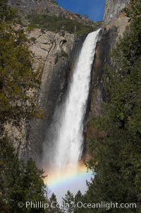 Bridalveil Falls with a rainbow forming in its spray, dropping 620 into Yosemite Valley, displaying peak water flow in spring months from deep snowpack and warm weather melt.  Yosemite Valley, Yosemite National Park, California