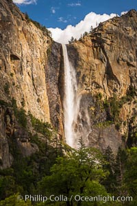 Bridalveil Falls at sunset, with clouds and blue sky in the background. Bridalveil Falls in Yosemite drops 620 feet (188 m) from a hanging valley to the floor of Yosemite Valley, Yosemite National Park, California