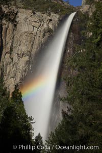 Bridalveil Falls with a rainbow forming in its spray, dropping 620' into Yosemite Valley, displaying peak water flow in spring months from deep snowpack and warm weather melt, Yosemite National Park, California