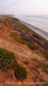 Eroding sandstone bluffs rise above a flat sand beach at sunset, small waves coming ashore, north of South Carlsbad State Beach