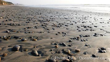 Cobblestones on a flat sand beach.  Cobble stones are polished round and smooth by years of wave energy.  They are alternately exposed and covered by sand depending on the tides, waves and seasons of the year.  Cobblestones are common on the beaches of southern California, contained in the sandstone bluffs along the beach and released onto the beach as the bluffs erode, Carlsbad