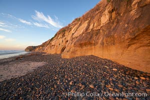 Cobblestones piled at the base of seacliffs, sunset.  Beach cliffs made of soft clay continually erode, adding fresh sand and cobble stones to the beach.  The sand will flow away with ocean currents, leading for further erosion of the cliffs, Carlsbad, California