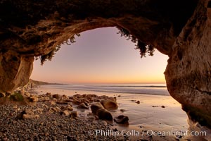 Sarah's Cavern, a natural sea cave hidden below sea cliffs in Carlsbad, opening onto a flat beach at sunset, inner walls adorned with graffiti.