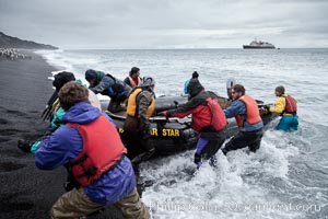Cheesemans Ecology Safaris tour leaders, work in the surf on a steep black sand beach at Bailey Head to assist tourists land ashore and handle the landing craft: an inflatable zodiac.  The icebreaker M/V Polar Star is anchored in the distance, Deception Island