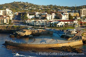 The Children's Pool in La Jolla, also known as Casa Cove, is a small pocket cove protected by a curving seawall, with the rocky coastline and cottages and homes of La Jolla seen behind it
