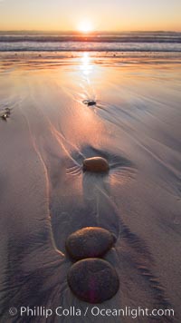 Cobblestone lies on the sand at the ocean's edge, sunset